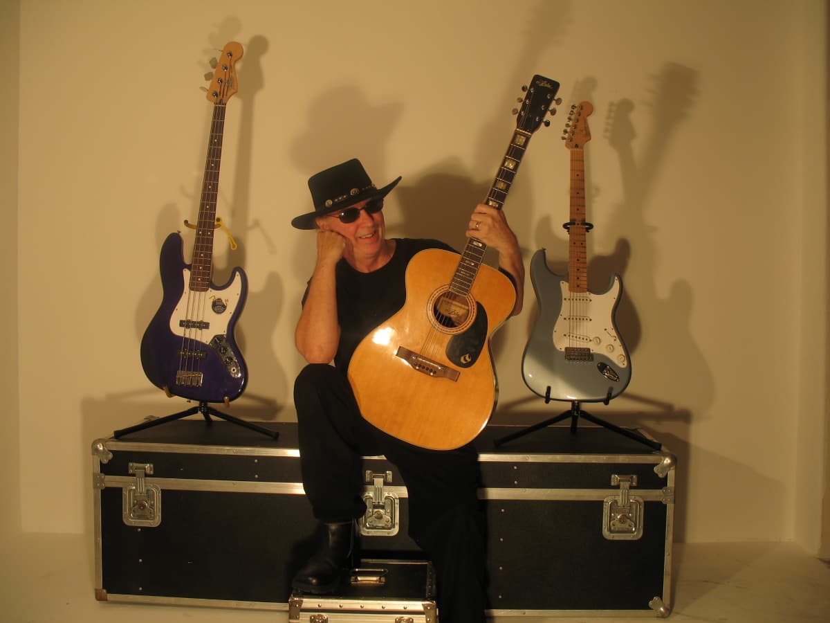 Dendee in Cowboy hat showing his collection of guitars