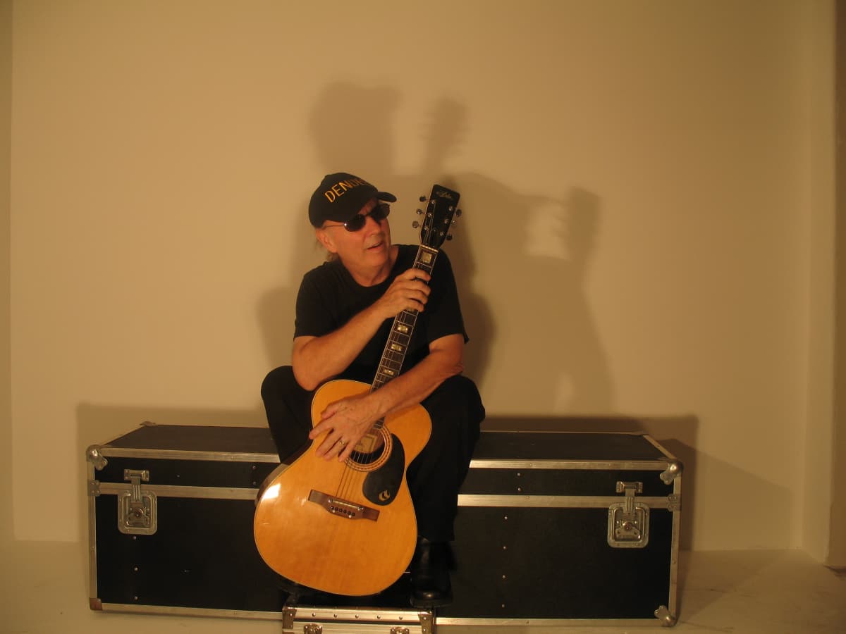 Dendee sitting with his Aria acoustic guitar